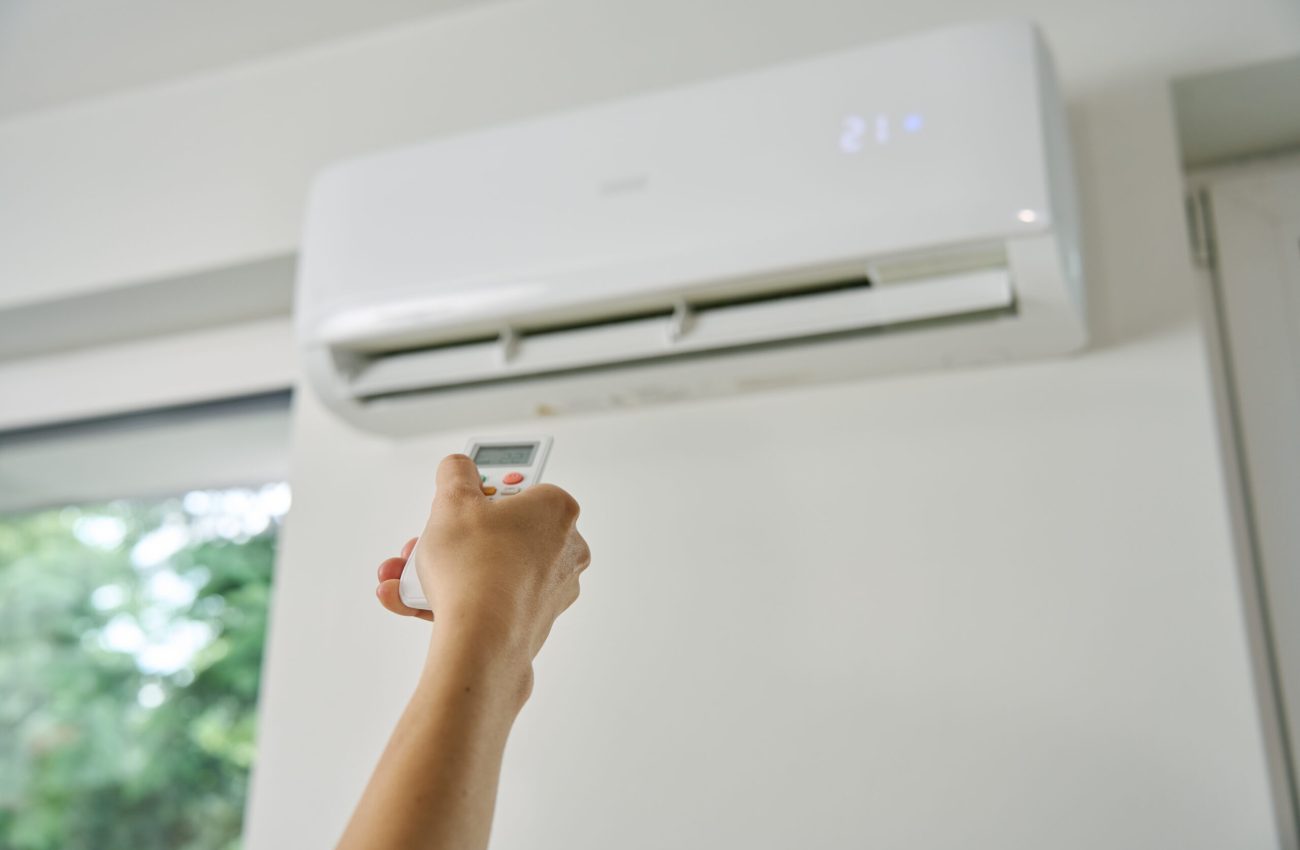 Adjusting Air Conditioner Temperature with Remote Control Adjusting air conditioner temperature with remote control. Hand holds remote control and setting comfortable temperature on climate system in apartment